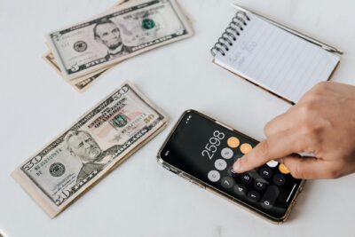 crop unrecognizable financier using calculator on smartphone near dollar banknotes